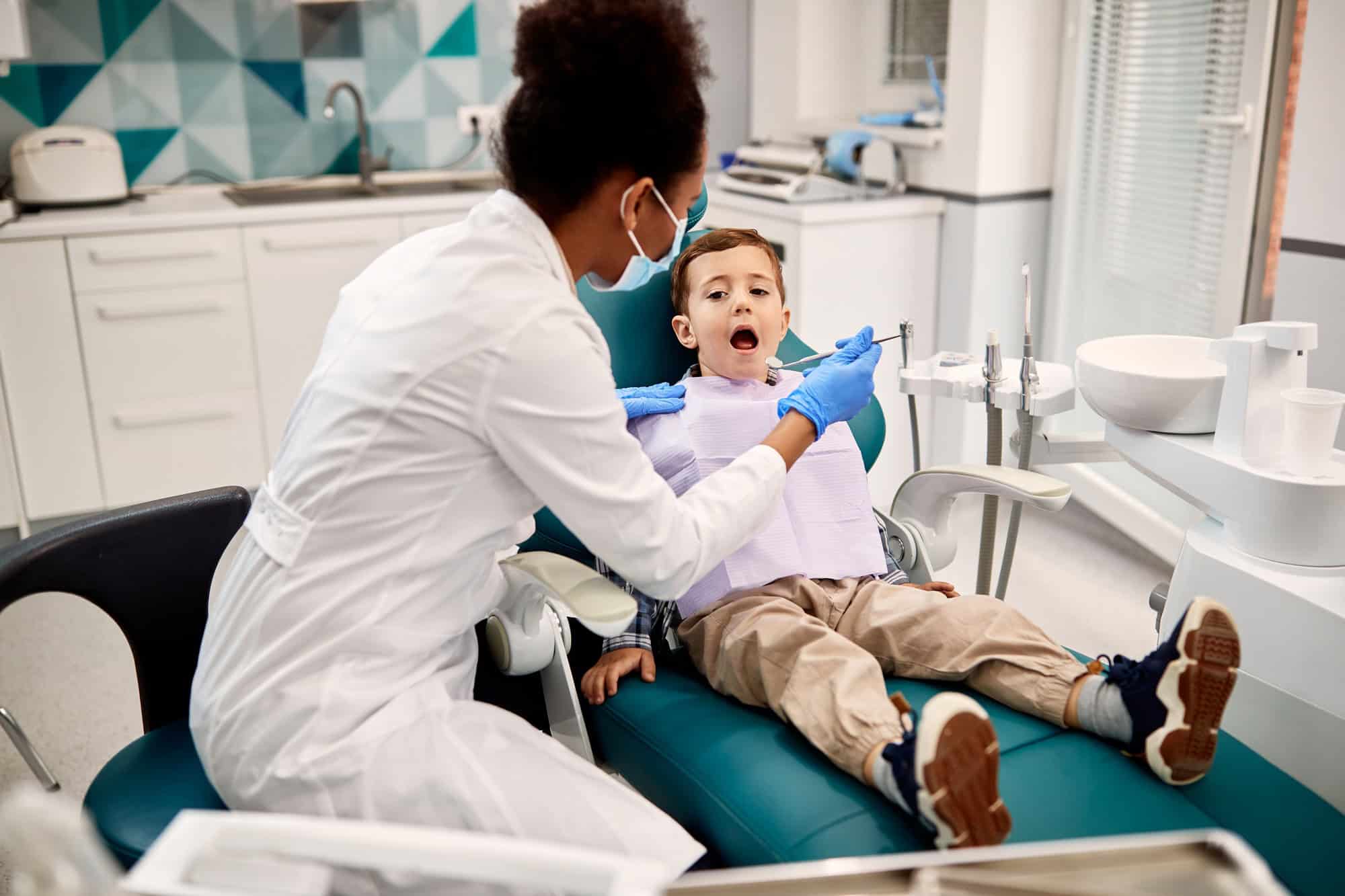 Black female dentist examining boy's teeth during appointment at dentist's office.