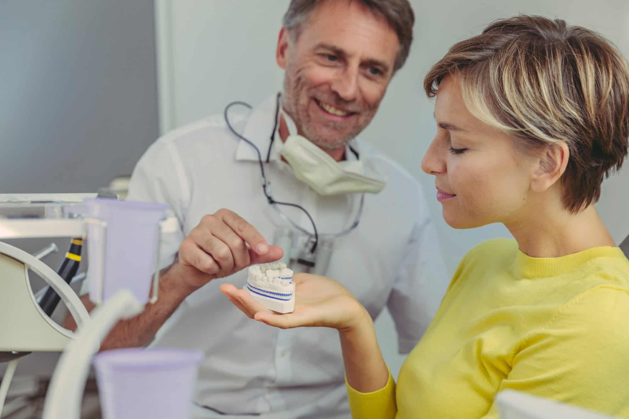 Dentist explaining dental bridg on a tooth model to his patient