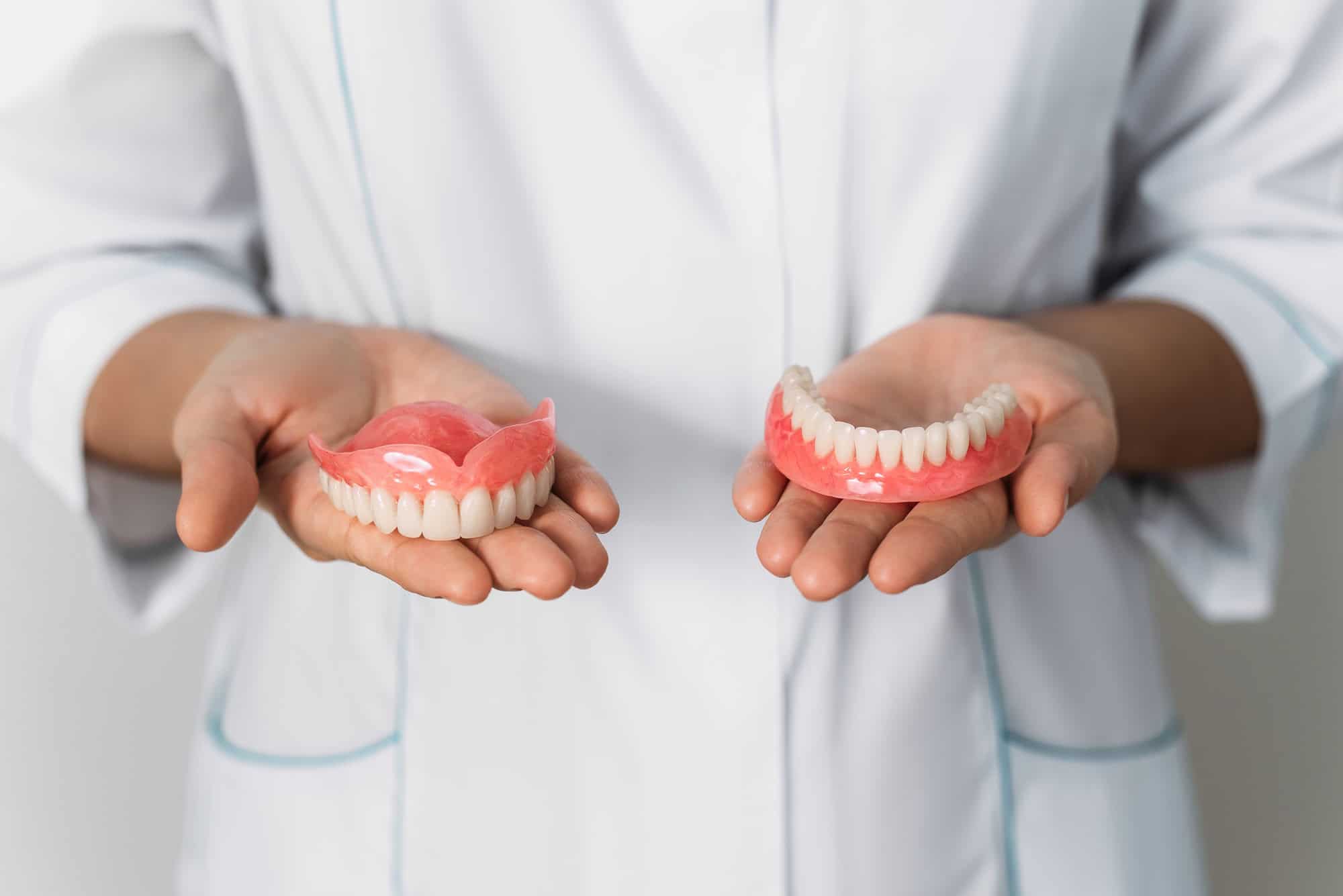 The dentist is holding dentures in his hands. Dental prosthesis in the hands of the doctor close-up